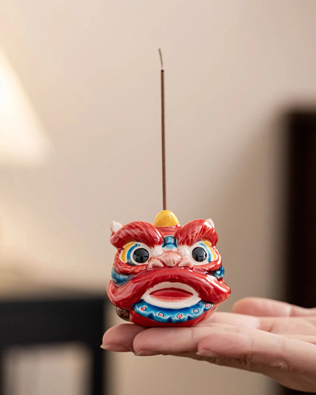 a red Lion-dance incense holder with an incense stick in hand