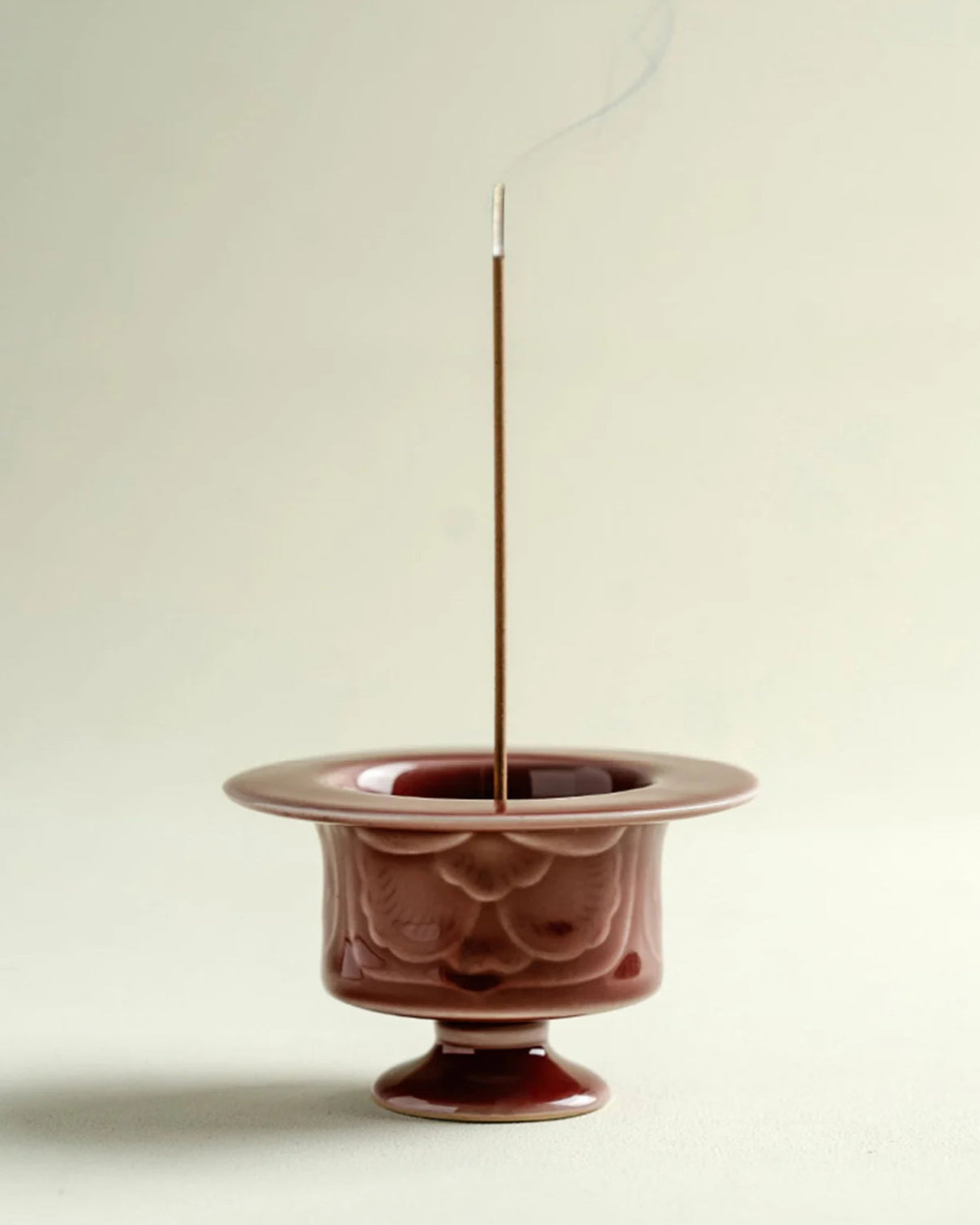 Ceramic incense burner with a single incense stick on a plain background