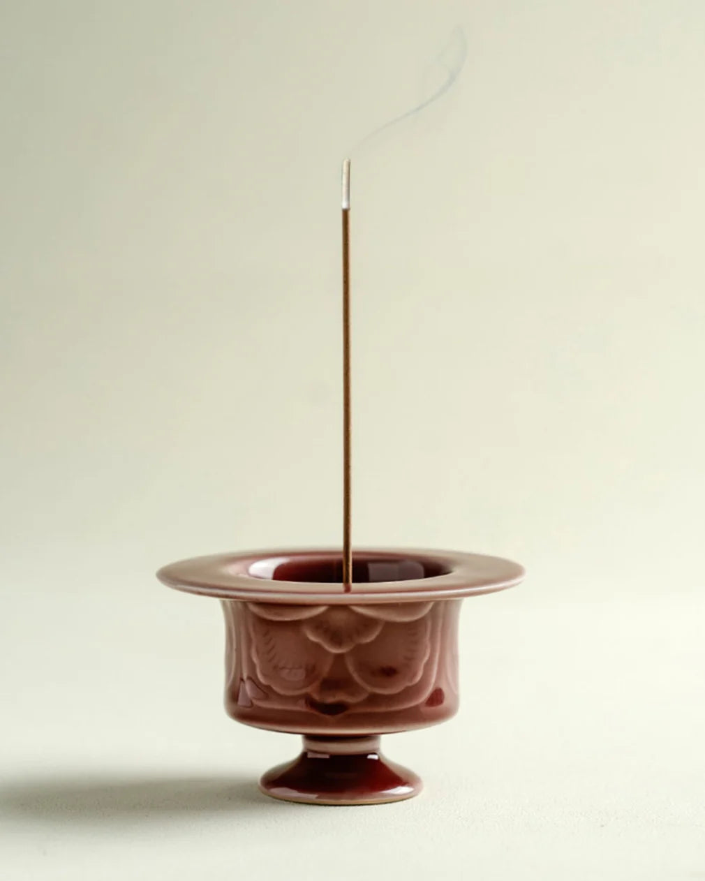 Ceramic incense burner with a single incense stick on a plain background