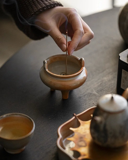 Person lighting incense in a small ceramic incense burner on a wooden table.