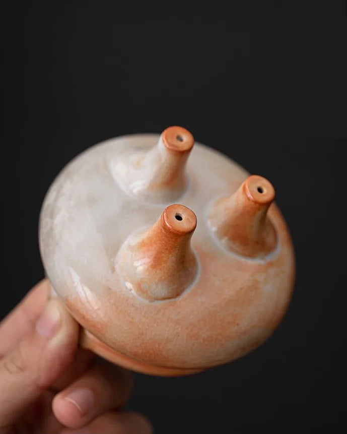 Ceramic incense burner with three nozzles held by a hand against a black background