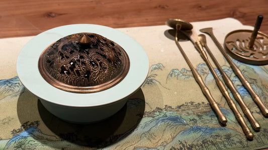 A traditional Chinese Xiangdao incense ceremony with a censer, pressed ash, and brass tools in a modern luxury study during morning golden hour.
