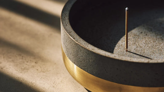 Close-up detail of a minimalist raw porcelain incense burner with a fine brushed brass inlay, showing a balance of Earth and Metal.