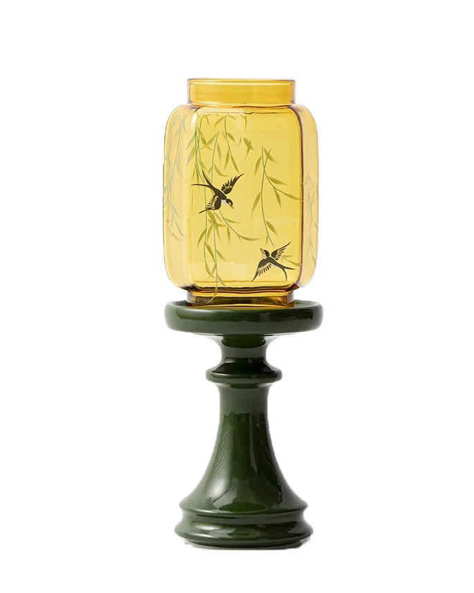 the eastern candle holder is yellow glass vase with swallow bird design on a green stand
