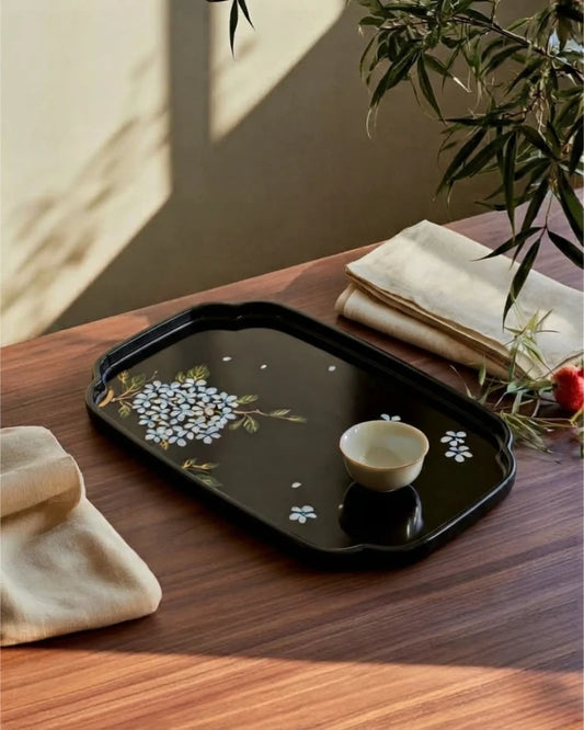 Hand-painted black bamboo lacquer tray with a floral motif and a tea cup on a wooden table