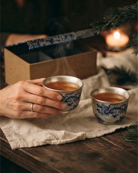 Azure Dragon tea cup pair beside an open patterned gift box, with one cup held in hand