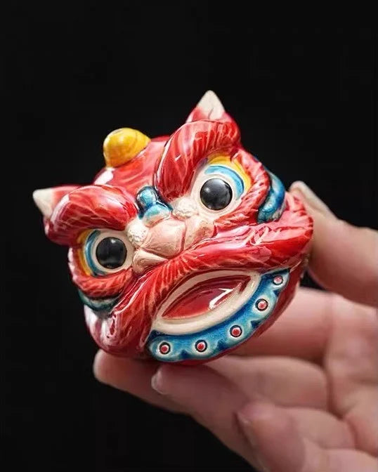 Colorful lion head figurine held in a hand against a black background