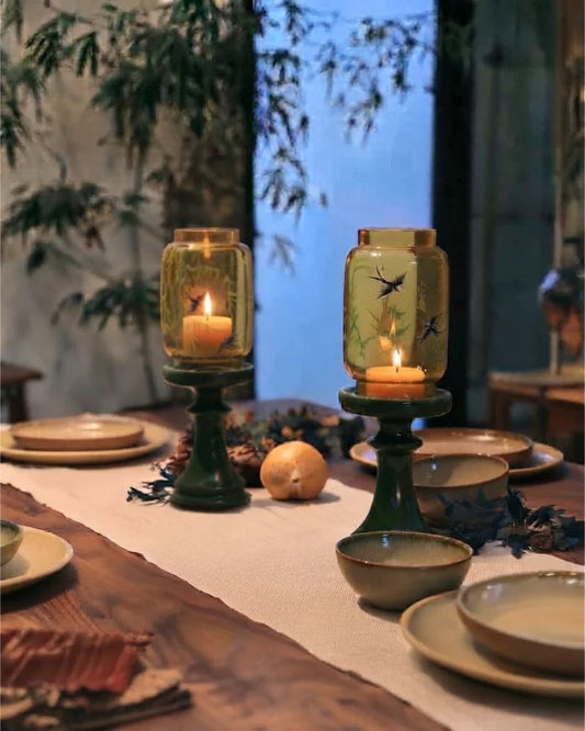 Pair of Imperial candle holders with green bases and glowing glass shades on a dining table