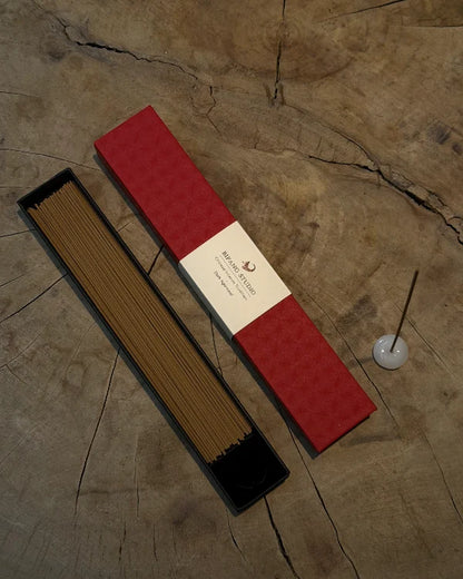 bifang studio chinese incense set displayed on a rustic wood surface, with an open black tray holding brown incense sticks, a red rectangular box with a cream label, and a small white incense holder with a stick.