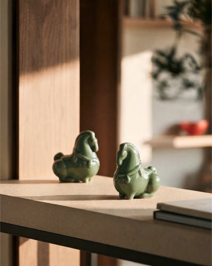 Two green celadon horse figurines displayed together on a sunlit wooden surface